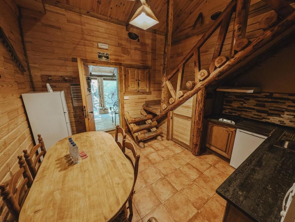 Een houten interieur met een eettafel, stoelen, een keukenhoek en een trap.