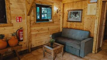 Un interior de madera con un sofá, una mesita con una planta, un extintor y una ventana con contraventanas.