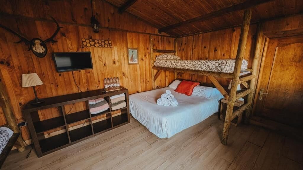 Ein Zimmer einer Holzhütte mit einem Etagenbett, einem kleinen Schreibtisch mit Lampe und einem an der Wand befestigten Fernseher.