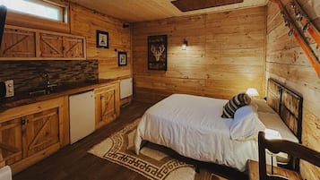 Interior de una cabaña de madera con una cama, una pequeña kitchenette y un soporte para esquíes.