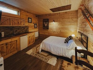 Interior de una cabaña de madera con una cama, una pequeña kitchenette y un soporte para esquíes.
