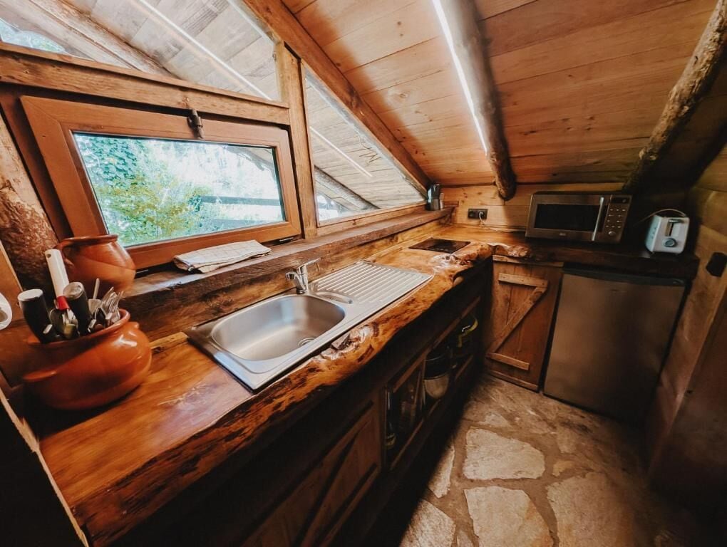 Eine rustikale Küche mit Steinboden, Holz Arbeitsplatten, einem Spülbecken, einer Mikrowelle und einem Fenster mit Blick auf Grünflächen.