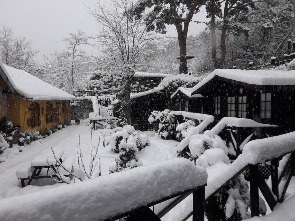 Un espacio exterior cubierto de nieve, con una valla de madera, un banco y un edificio con techo inclinado.