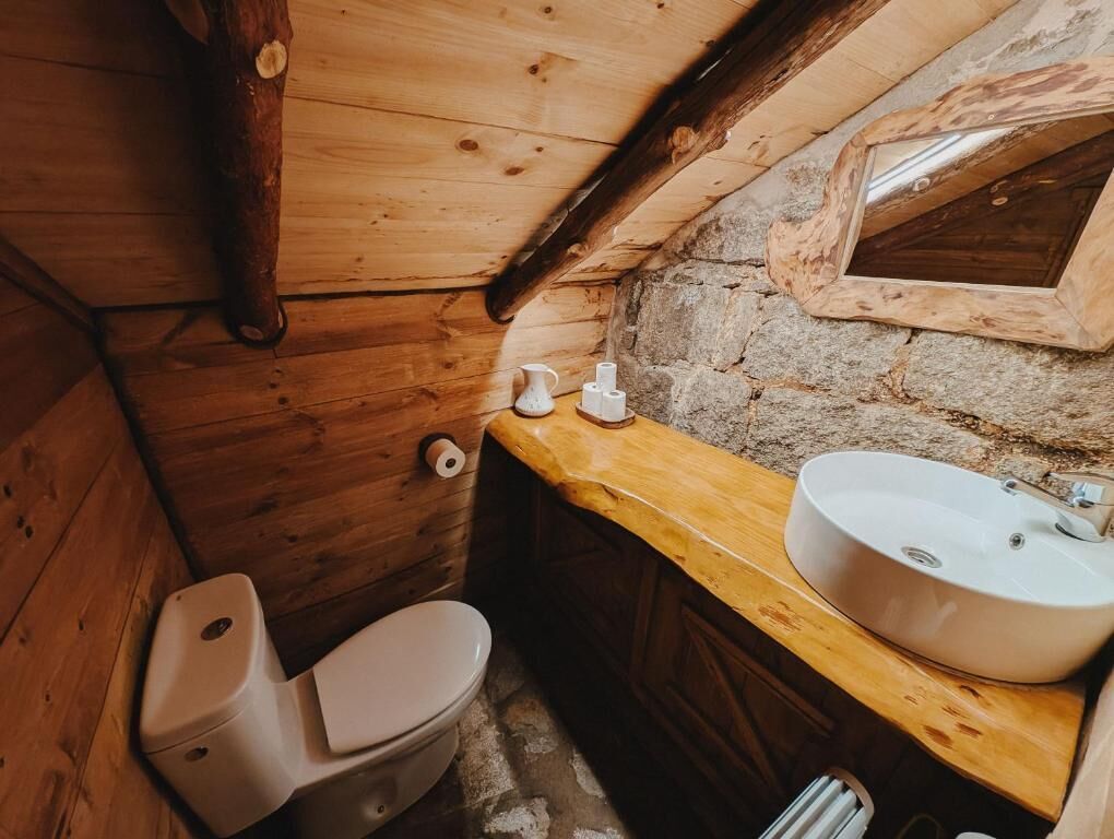 A wooden cabin bathroom with a toilet, sink, and a stone wall.