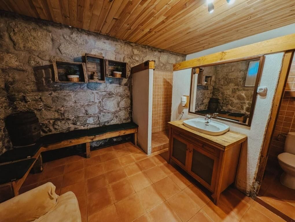Ein rustikales Badezimmer mit Steinwand, Holzbank, Waschtisch mit Becken und Spiegel.
