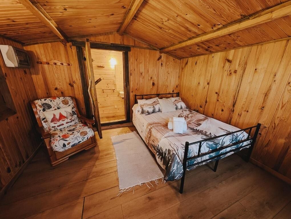 A wooden room with a bed, a chair, and a door.