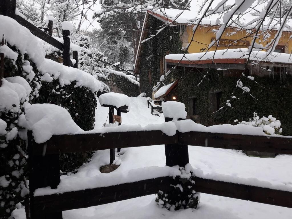 Un espacio exterior cubierto de nieve, con una valla de madera, un banco y un edificio al fondo.