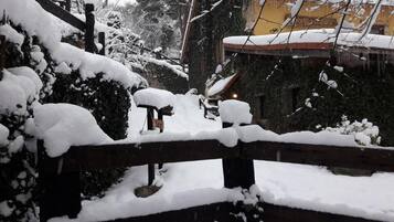 Un espacio exterior cubierto de nieve, con una valla de madera, un banco y un edificio al fondo.