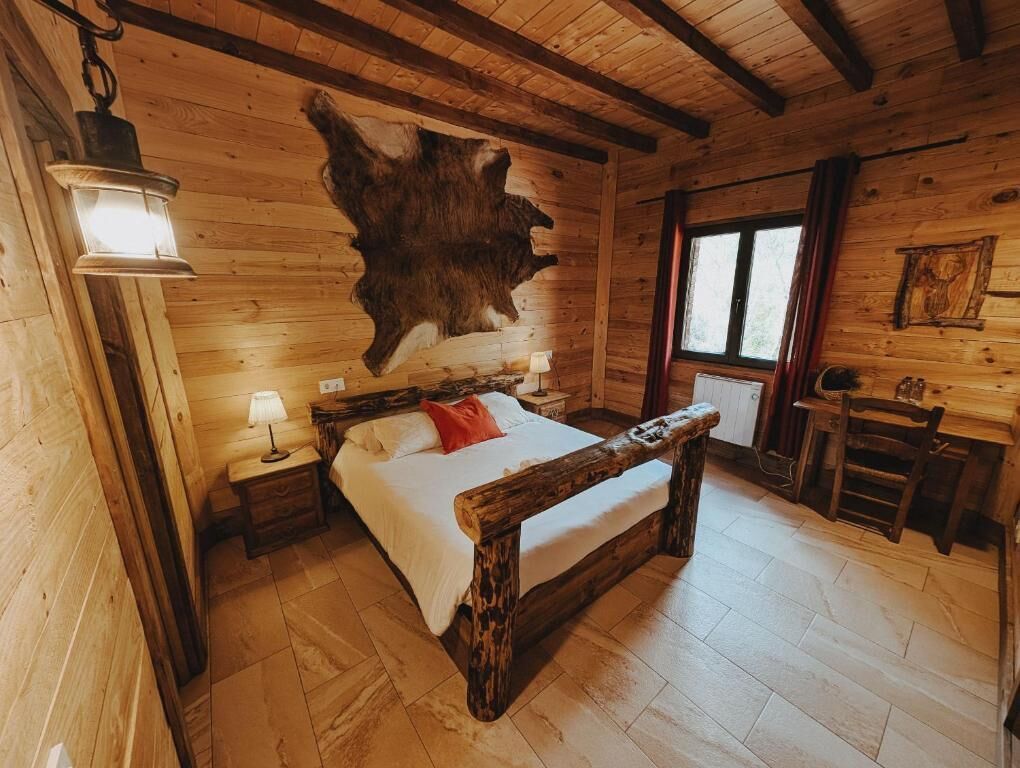 Een houten kamer met een bed, een dierhuid aan de wand, een bureau en een raam.
