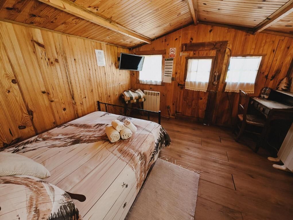 A wooden cabin room with a bed, a desk, and a television.