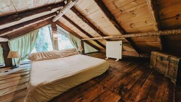 Una habitación con suelo de madera, una cama con ropa blanca, un radiador y una ventana con cortinas.