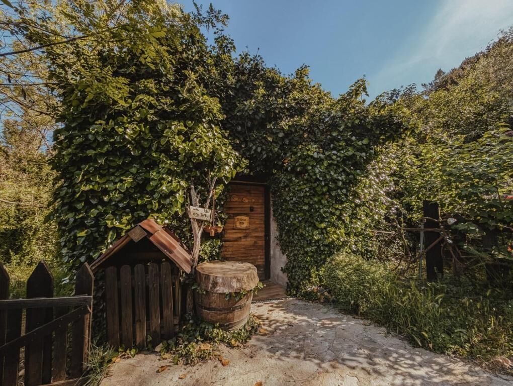 Un edificio de madera rústico con un letrero, un barril y una valla de madera en un jardín.