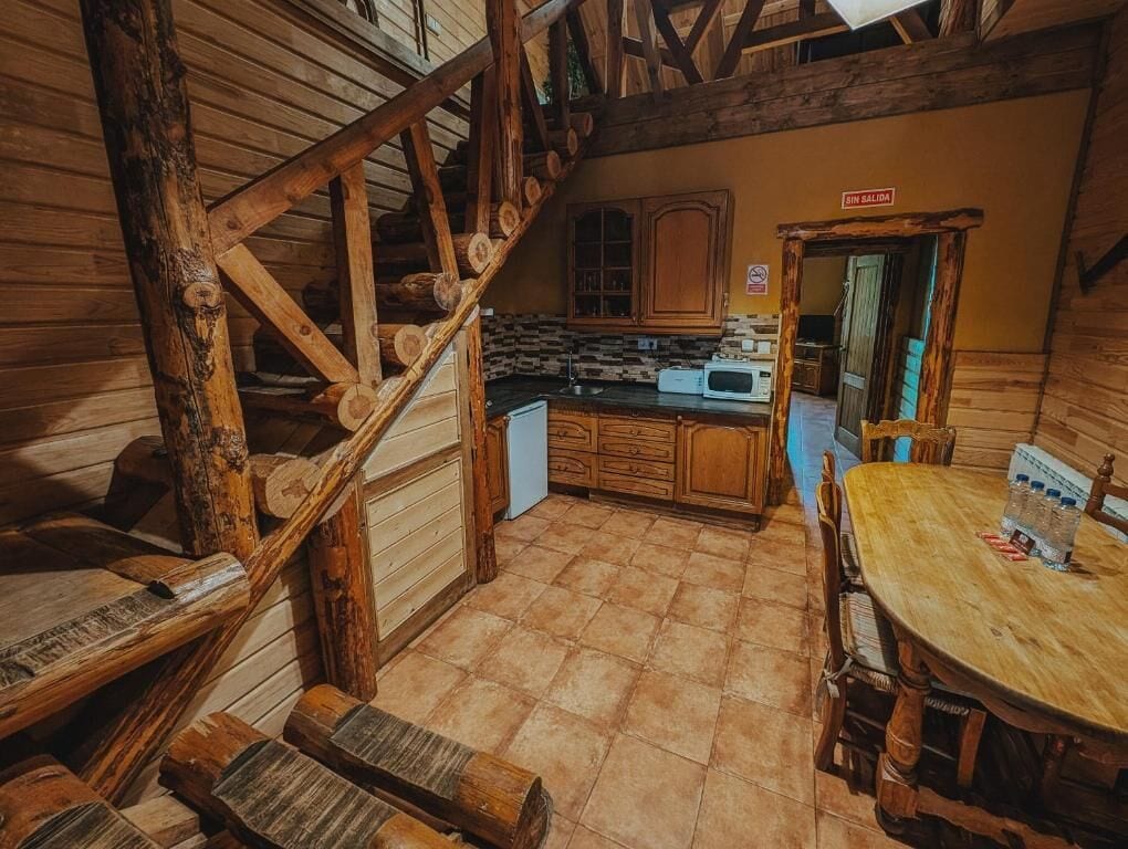 A rustic wooden interior with a kitchen area, a dining table, and a staircase.