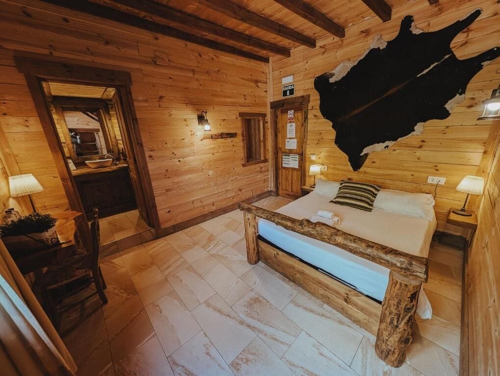 Habitación de cabaña de madera con una cama, un banco de madera y un tapiz de cuero de vaca en la pared.