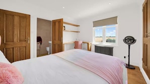 A bedroom with a large bed, a window with a view, a radiator, and a standing fan.