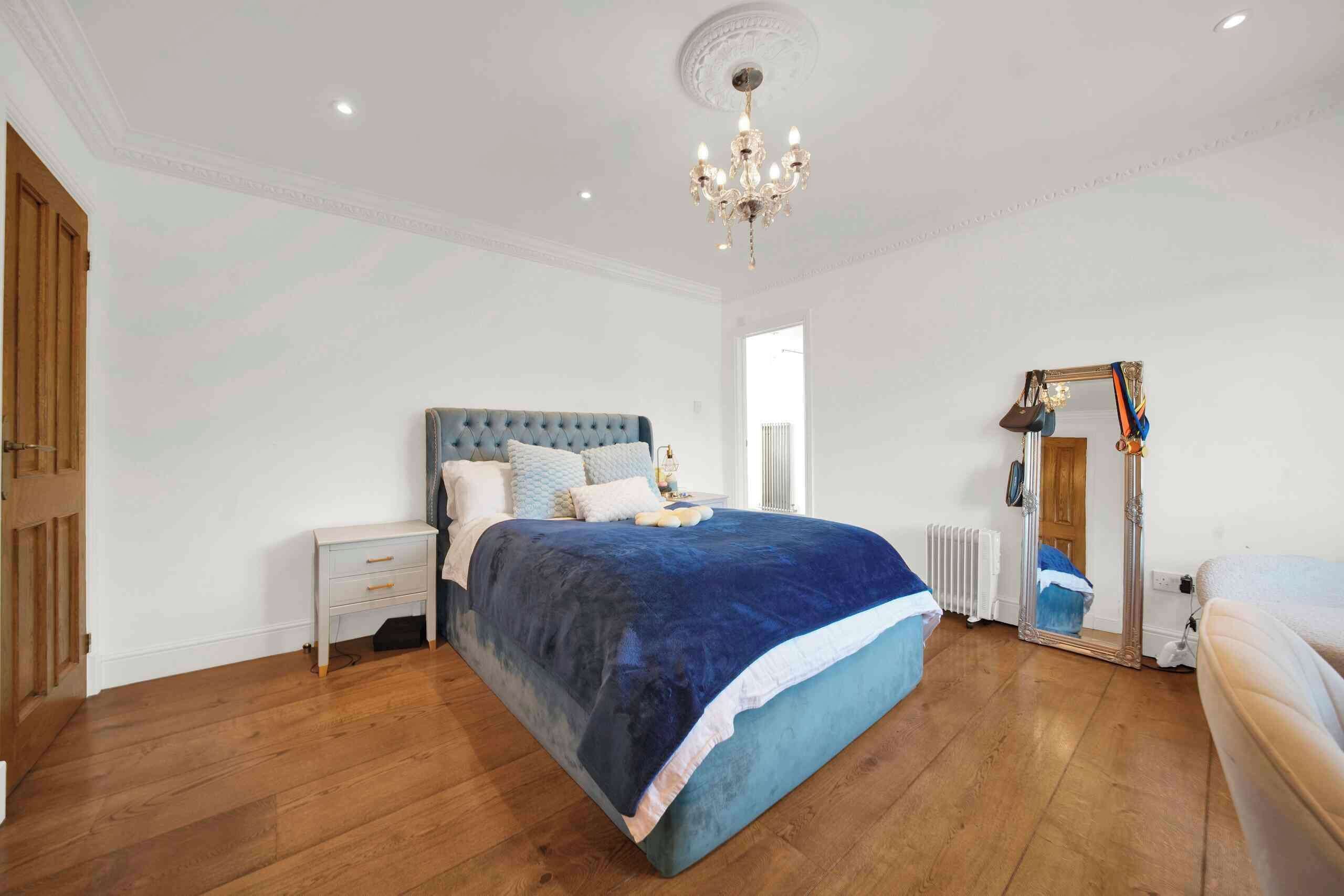 A bedroom with a large bed, a nightstand, a dresser, a mirror, and a chandelier.