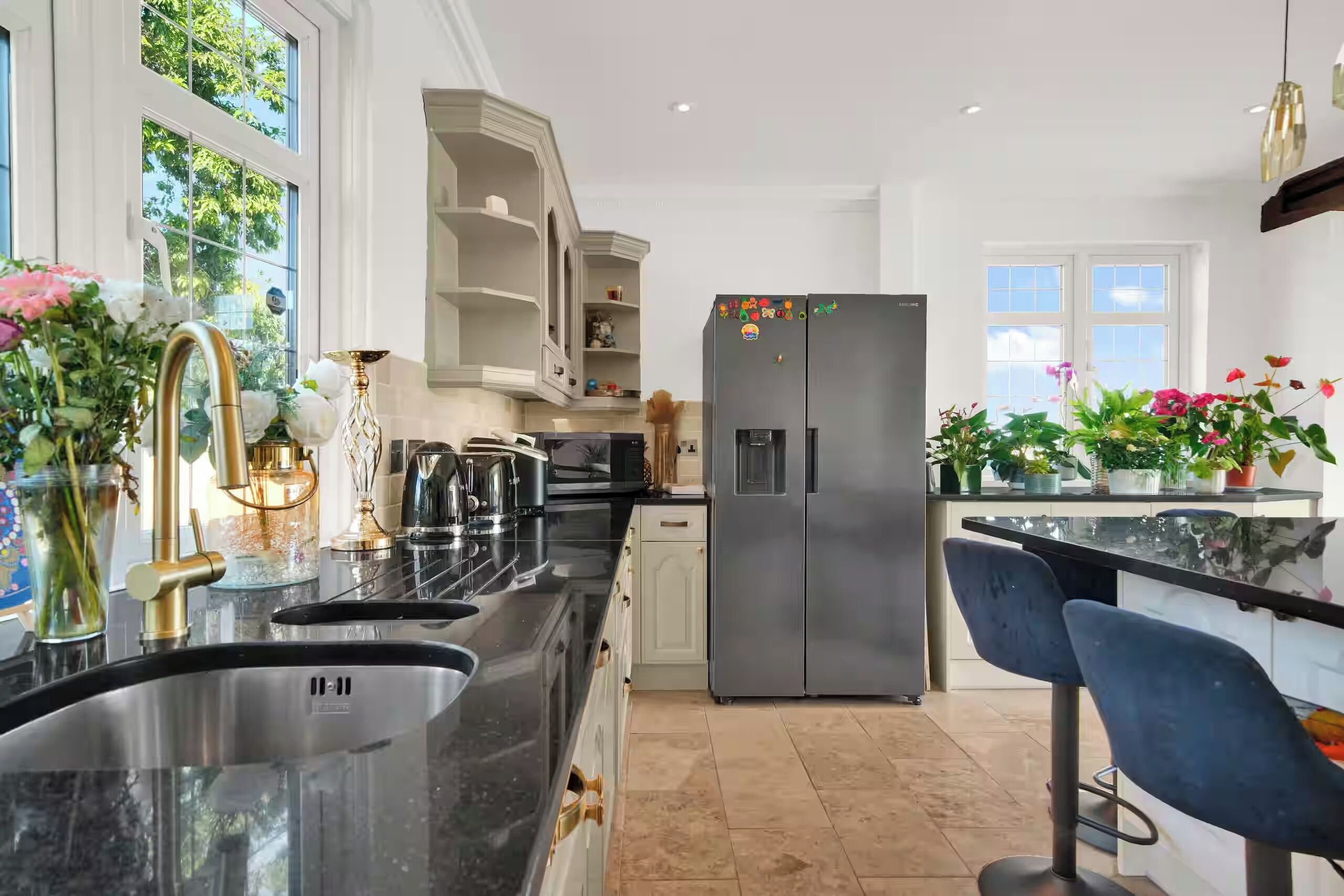 Eine moderne Küche mit einem Edelstahlkühlschrank, einer Spüle mit zwei Becken und einer Bar mit einem Barhocker.