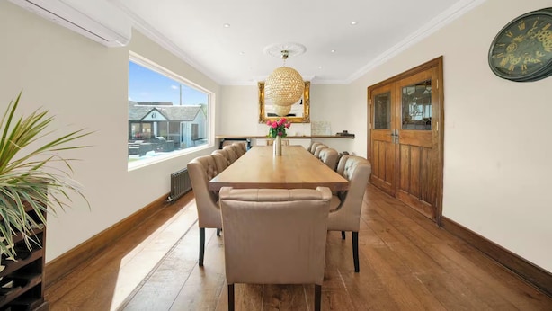 A spacious dining area with a long wooden table, leather chairs, and a chandelier.