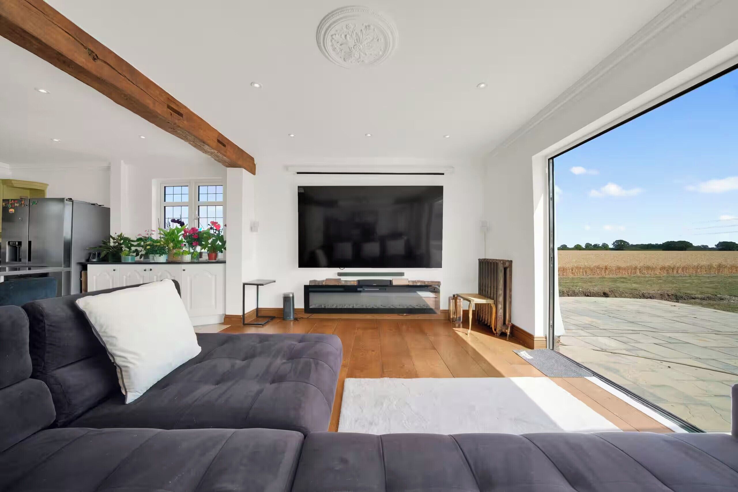 Ein modernes Wohnzimmer mit einem großen Flachbildfernseher, einem grauen Sofa und einem Holzbalken an der Decke.