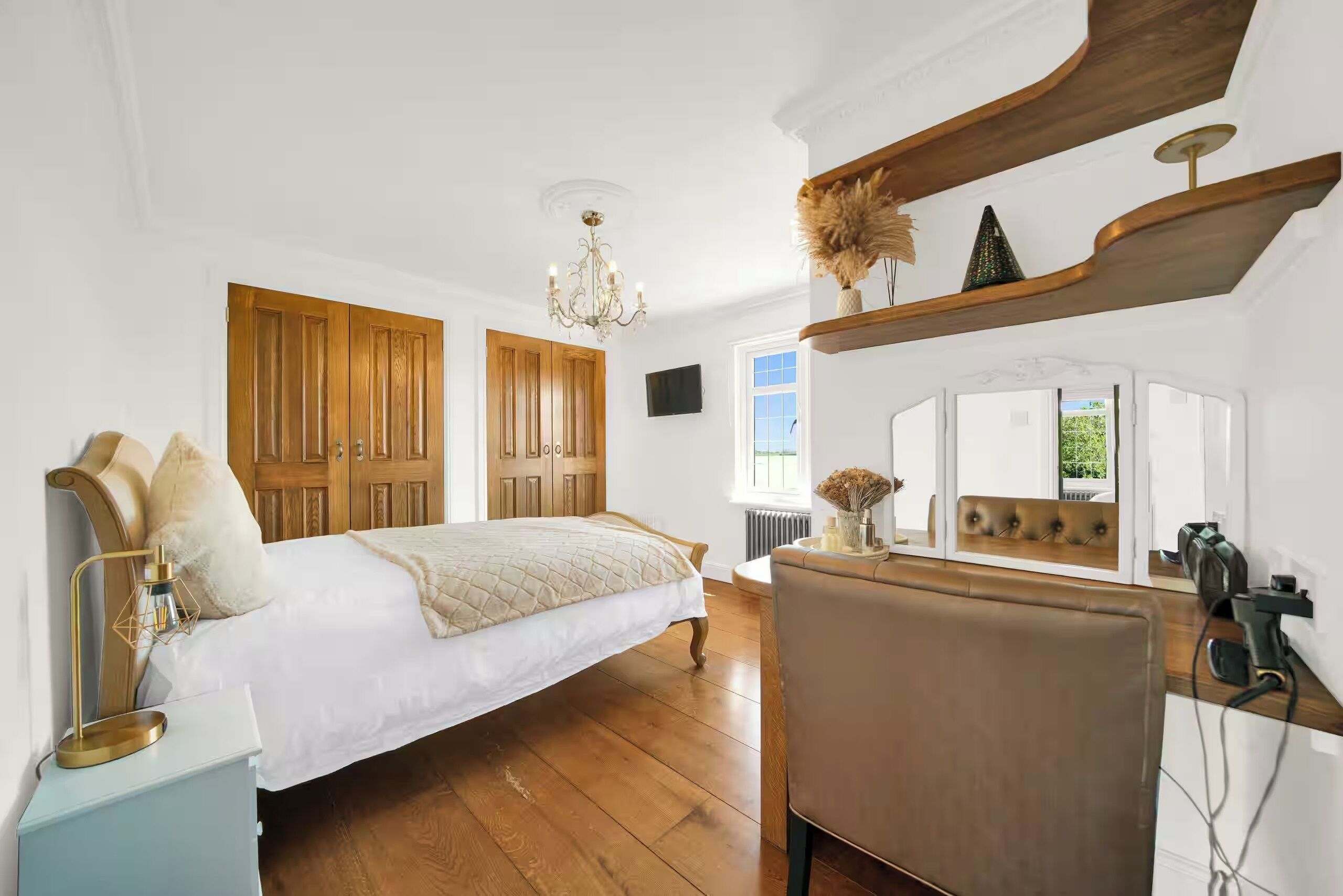 A bedroom with a large bed, wooden wardrobe, chandelier, and a view of the outdoors.