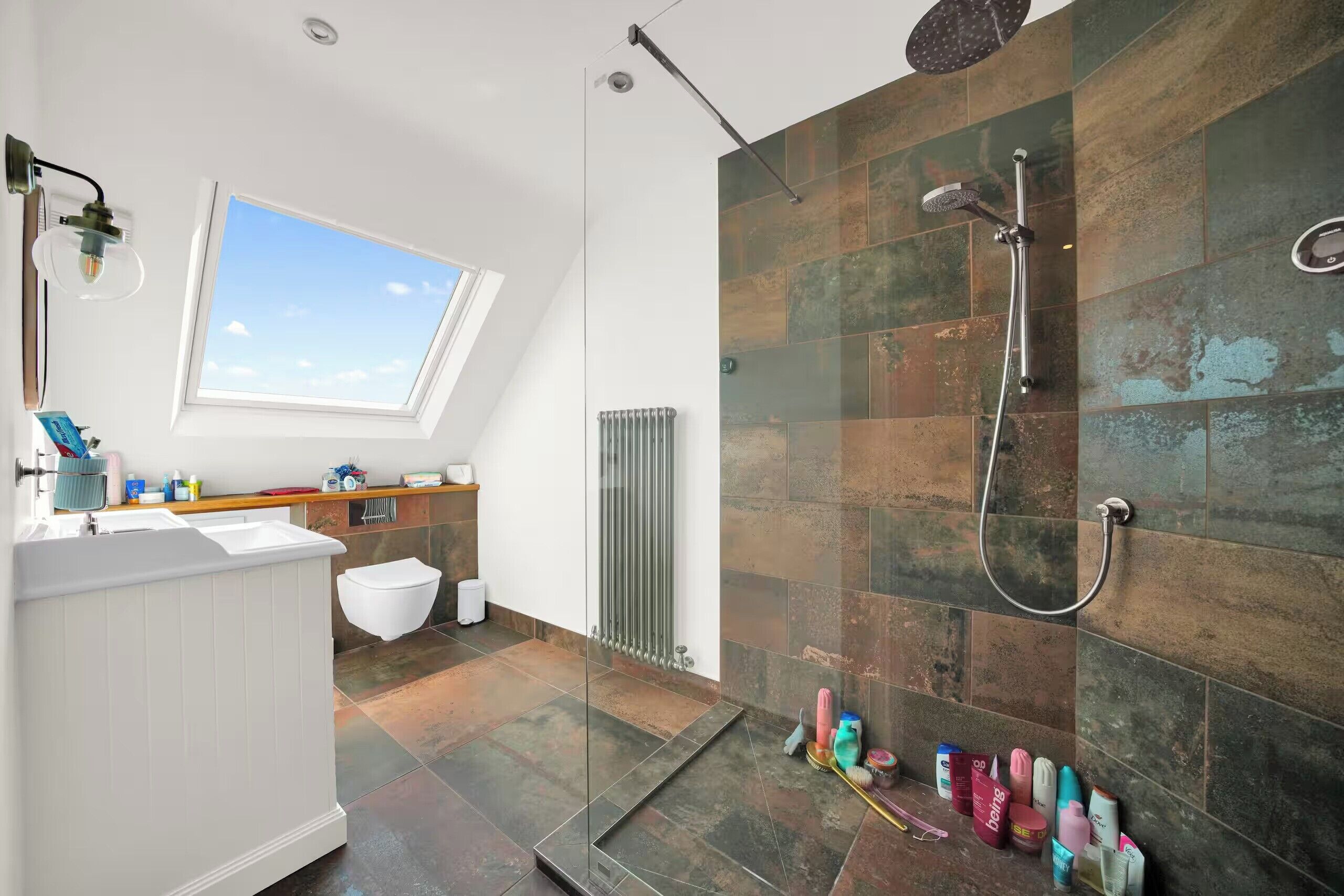 Een moderne badkamer met dakraam, een douche met regendouche en diverse toiletartikelen op het aanrecht.