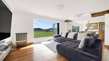 A modern living room with a large grey sectional sofa, a wooden floor, and a view of a grassy area through a glass door.