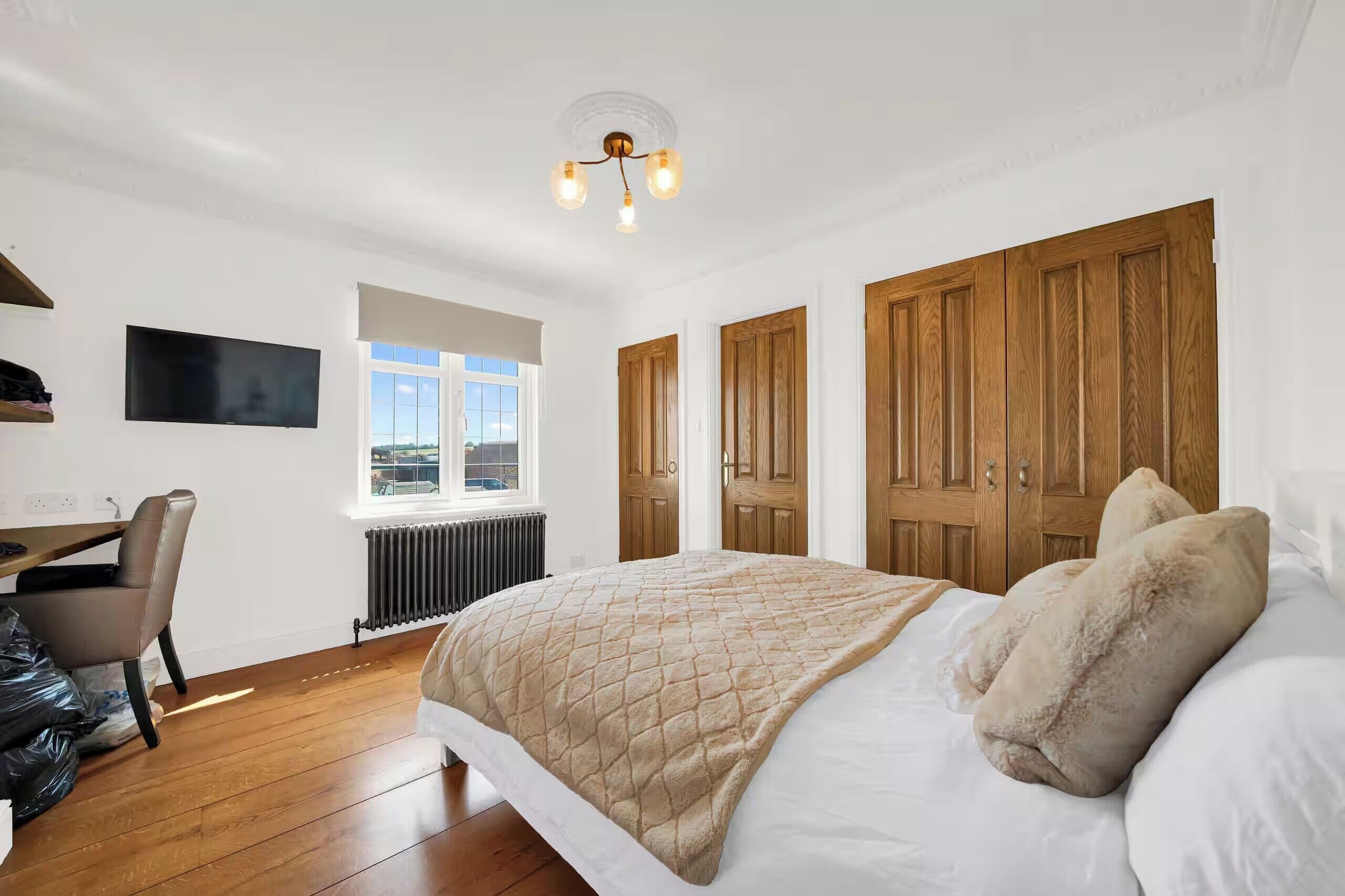 Un dormitorio con cama, escritorio, silla, radiador, televisor y ventana.