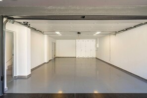 A clean, empty garage with a polished floor, white walls, and a set of double doors in the center. - Exclusive  private villa with endless ocean views (Adeje)
