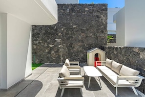 Ein moderner Außenbereich mit Sitzgelegenheiten, einem Mauerwerk im Hintergrund, einem kleinen Hundehäuschen und minimalistischem Design.
