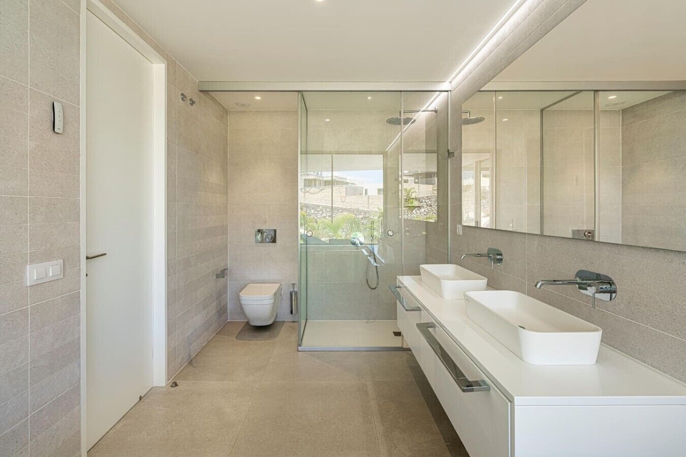 A modern bathroom with a glass-enclosed shower, a toilet, and a vanity with two sinks.