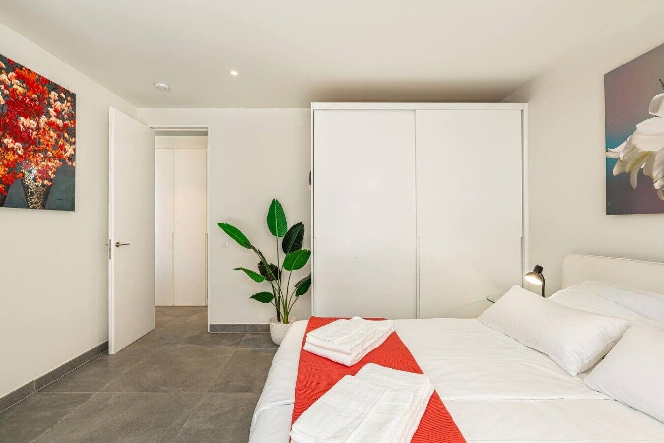 A hotel room with a bed, a potted plant, and artwork on the walls.