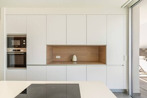 A modern kitchen with built-in appliances, a wooden shelf, and a view of the outdoors. - Exclusive  private villa with endless ocean views (Adeje)