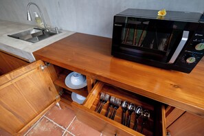 Una cocina con microondas en la encimera, un fregadero y un cajón con utensilios.