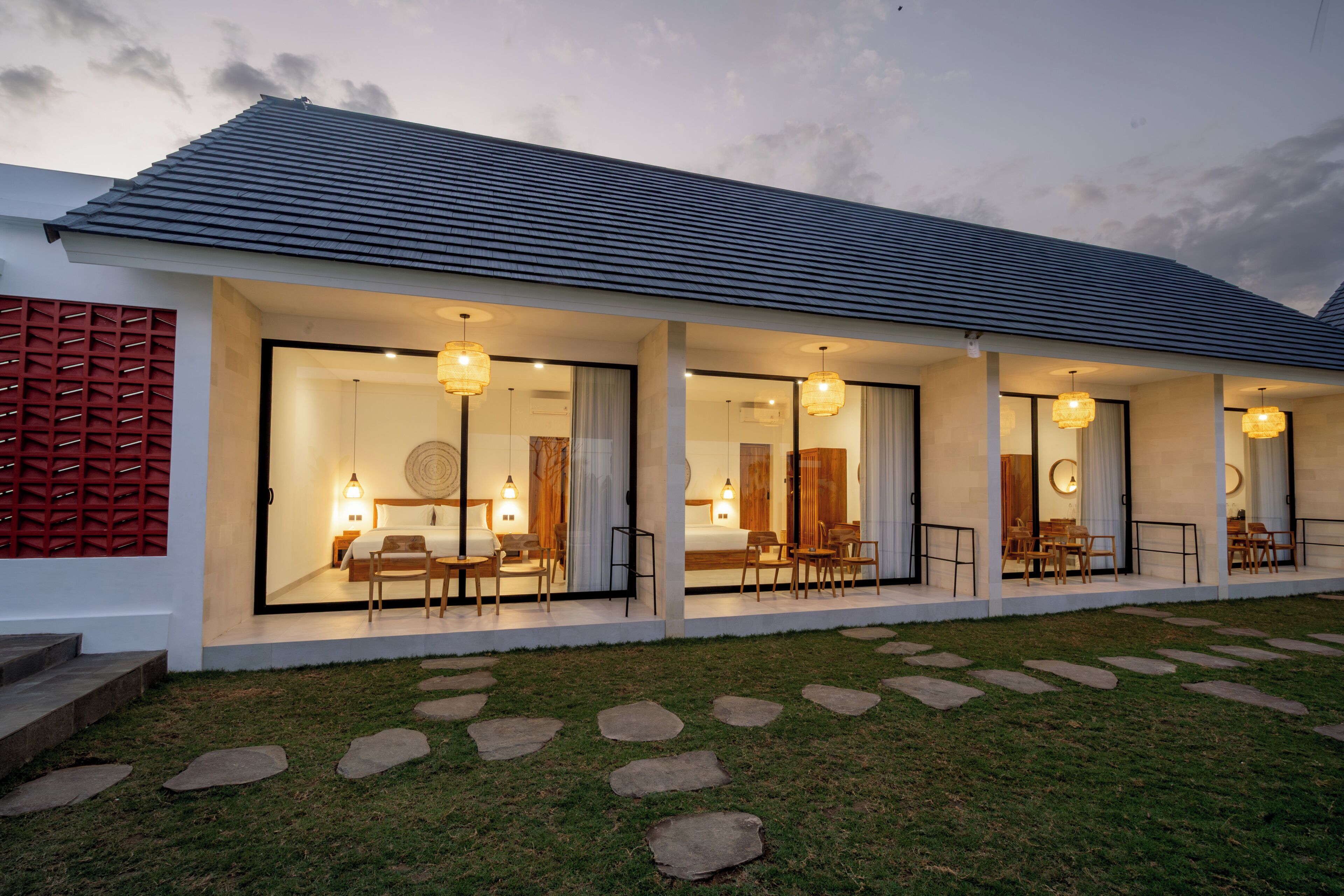 A modern hotel with a covered outdoor seating area, large windows, and a well-maintained lawn.