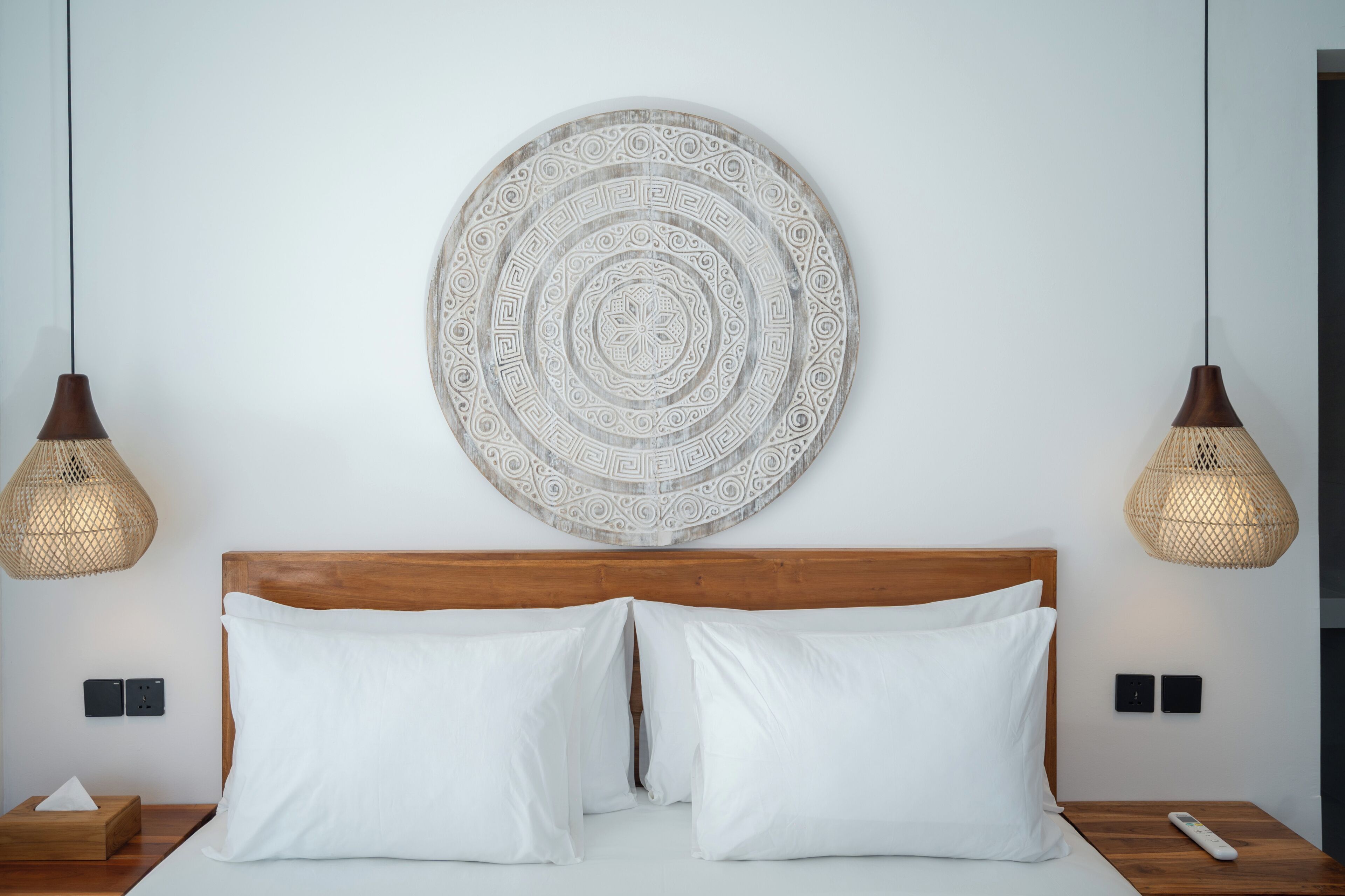 A bedroom with a wooden headboard, two bedside lamps, a wall-mounted decorative plate, and a bedside table with a remote control.