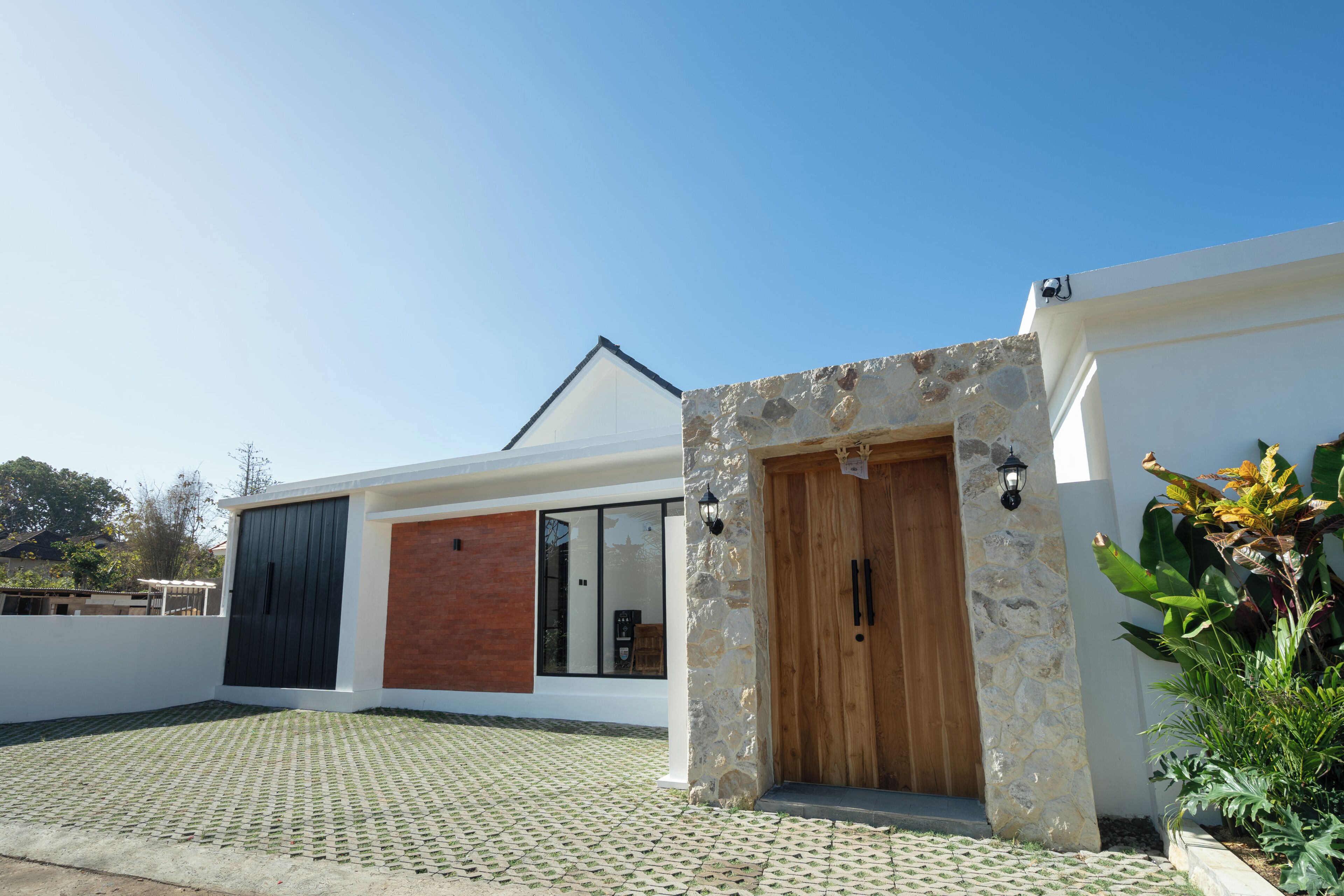 A modern house with a stone entrance, a large window, and a paved driveway.