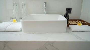 A bathroom with a white rectangular sink, two glass bottles, a faucet, a soap dispenser, and a wooden tray with towels.
