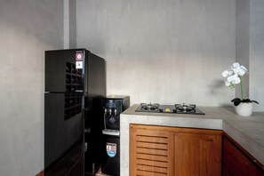 A compact kitchen with a refrigerator, a water dispenser, a stove, and a potted orchid.