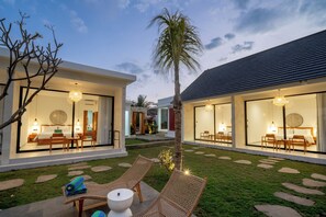 A modern hotel with two guest rooms, each with a large glass door, a dining area, and a small outdoor seating area with wicker furniture.