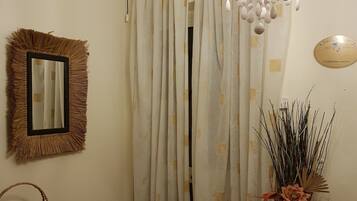 A room with a chandelier, a mirror, a curtain, a vase with dried plants, a wooden table, and a chair.