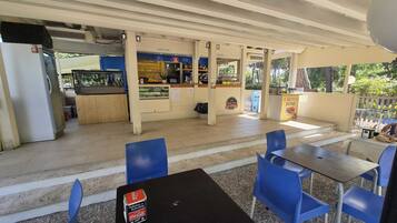 An outdoor cafe with blue chairs and tables, a Coca-Cola cooler, and a crepes zone.
