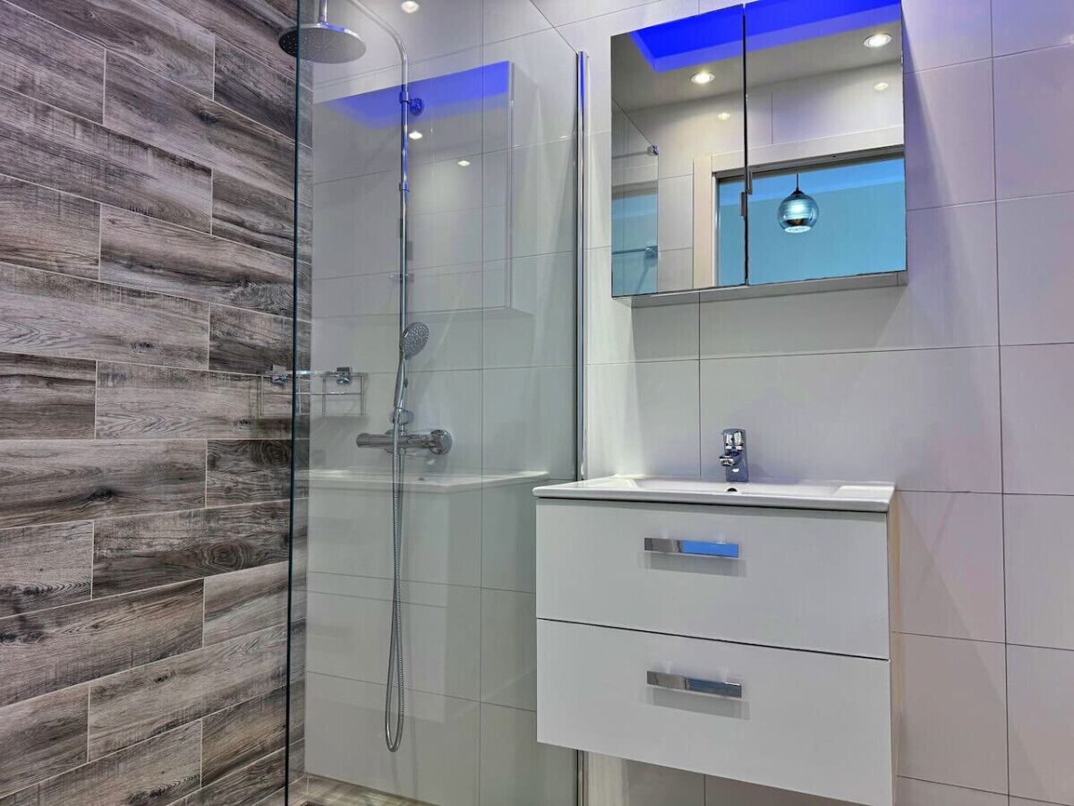 Une salle de bain moderne avec une douche à parois de verre, un meuble-lavabo blanc et un miroir au-dessus du lavabo.
