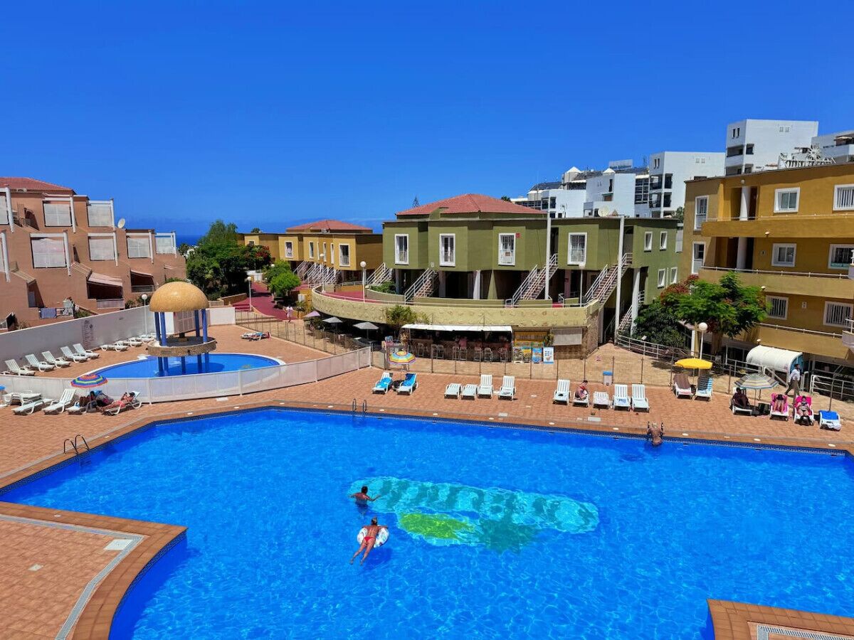 Ein Pool mit Liegestühlen und einem überdachten Bereich, umgeben von mehrstöckigen Gebäuden mit Balkonen.