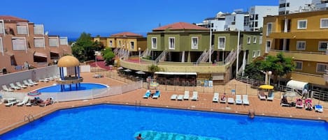 Ein Pool mit Liegestühlen und einem überdachten Bereich, umgeben von mehrstöckigen Gebäuden mit Balkonen.