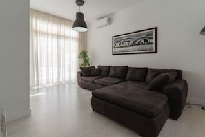 A modern living room with a sectional sofa, a large window with sheer curtains, a floor lamp, and a framed picture on the wall. - Nice Bungalow with Two Bedrooms (Playa de la Américas)