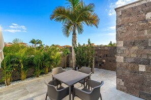 Un patio al aire libre con una mesa y sillas, rodeado de plantas y un muro de piedra.