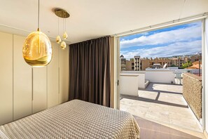 Een slaapkamer met een bed, een hanglamp en een uitzicht op een stadsgezicht door een schuifdeur.