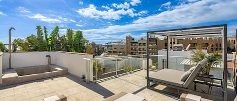 A rooftop terrace with a glass balustrade, outdoor seating, and a view of the cityscape.