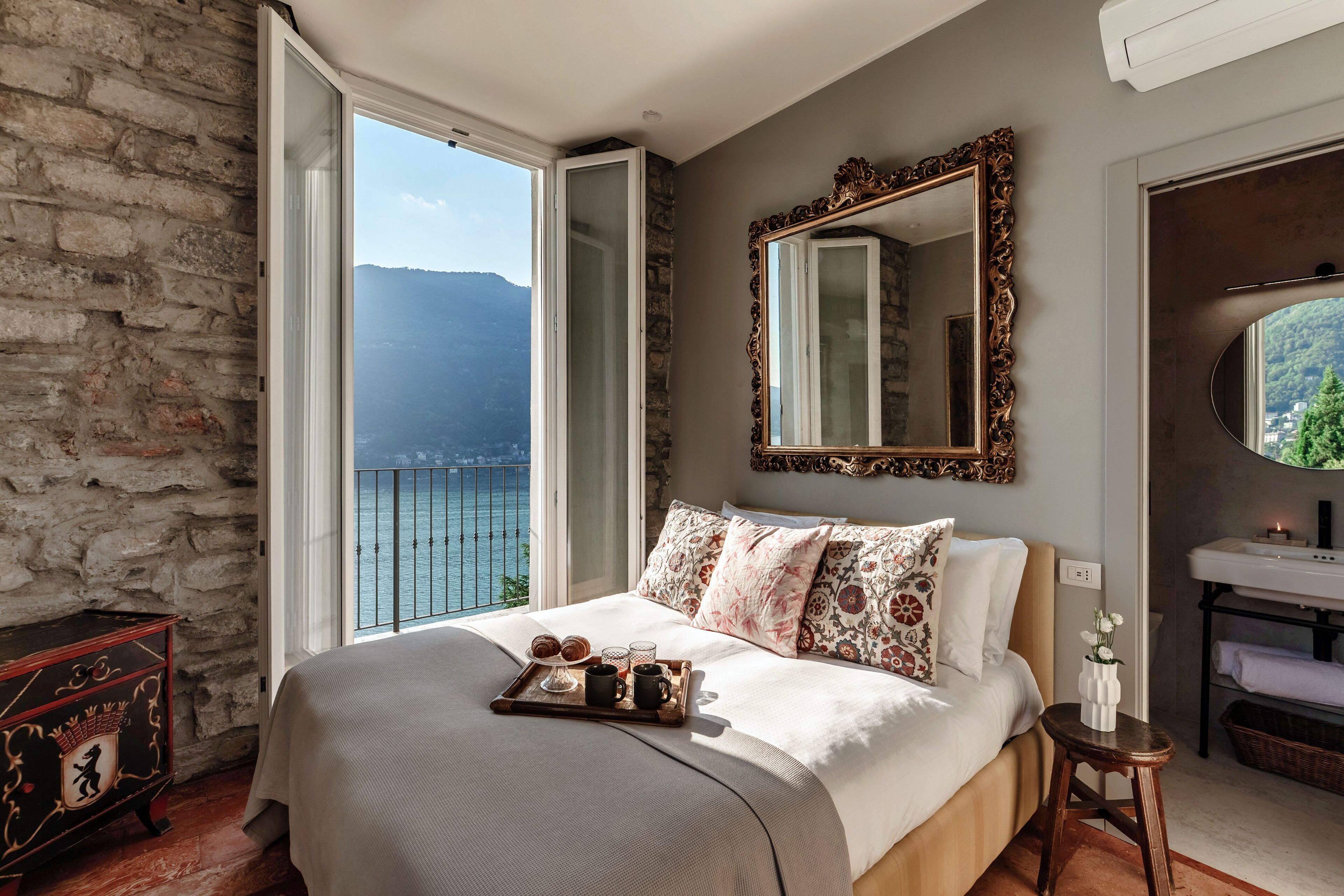 A bedroom with a bed, a dresser, a mirror, and a view of a body of water.