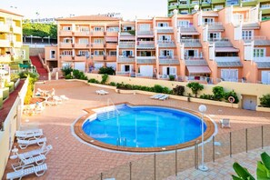 A swimming pool with sun loungers and a view of multi-story buildings. - 1bedroom ocean view apartment (Costa Adeje)